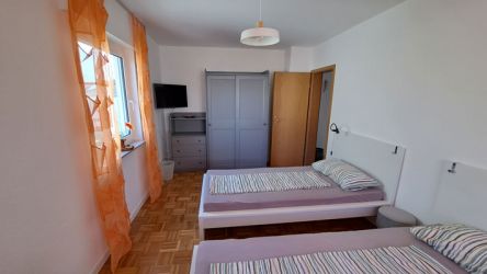 Freundliches Schlafzimmer mit zwei Einzelbetten, grauem Kleiderschrank und Fernseher in der Ferienwohnung.