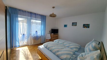 Helles Schlafzimmer mit Doppelbett, blauen Vorhängen und moderner Einrichtung in der Ferienwohnung.