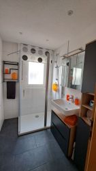 Modernes Badezimmer mit großer Dusche, Waschtisch und hellen Fliesen in der Ferienwohnung.
